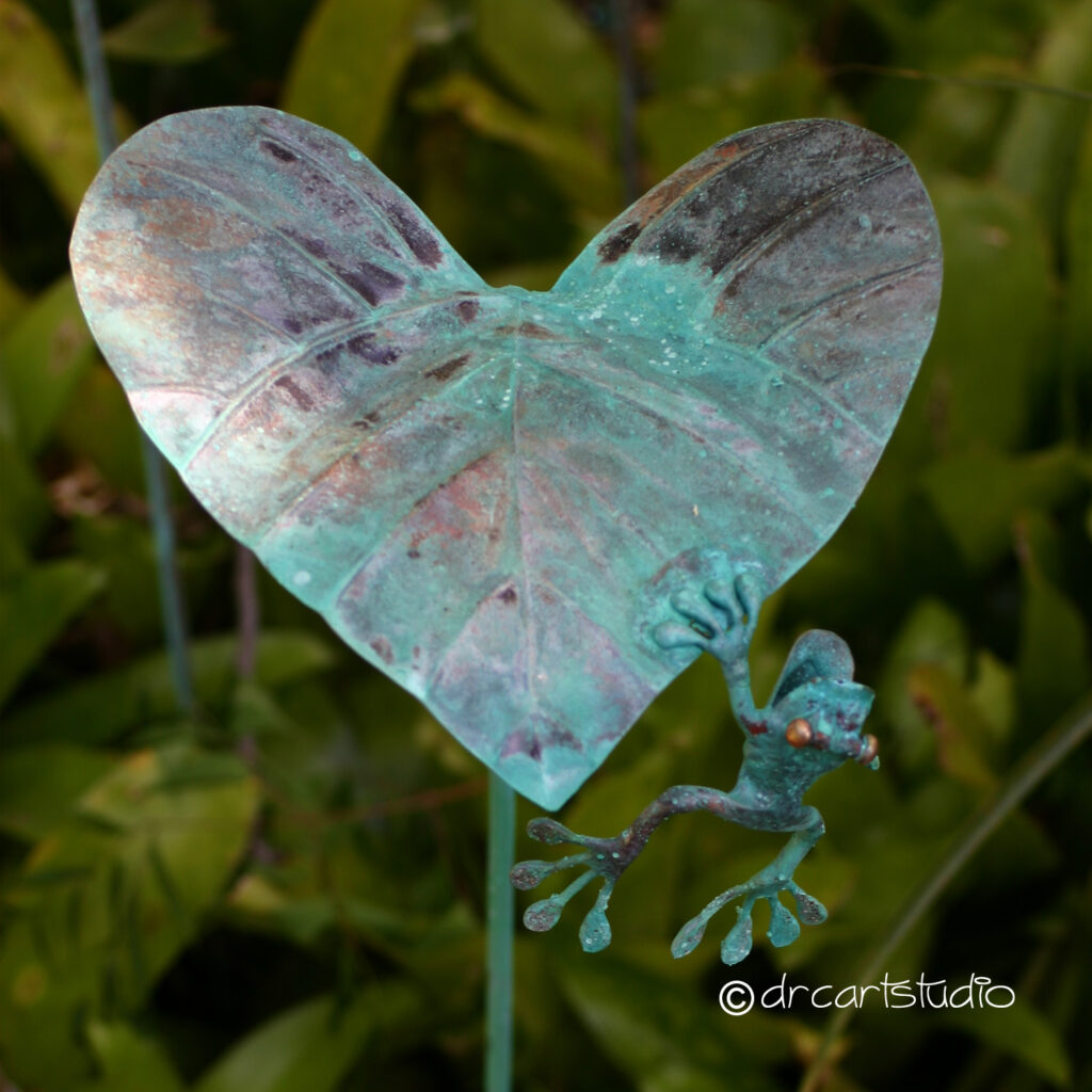 Photo of a hand made copper frog, trying to climb on a leaf.