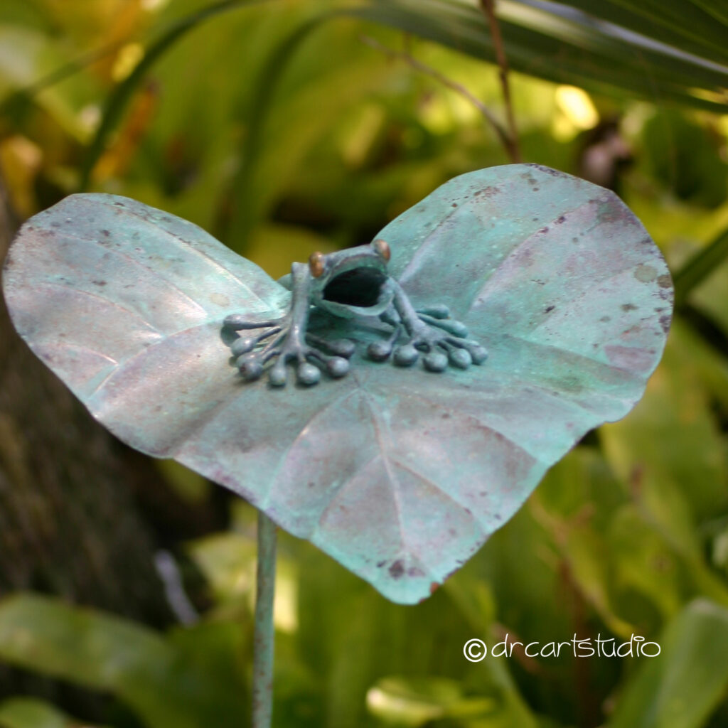 Photo of a hand made copper frog, sitting on a leaf.