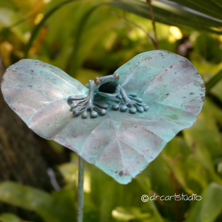 Photo of a hand made copper frog, sitting on a leaf.