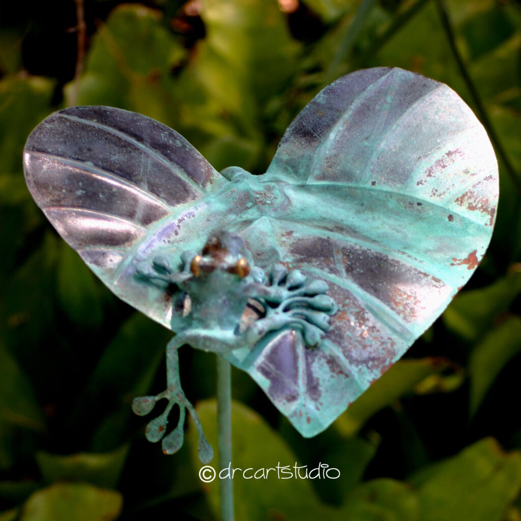 Photo of a hand made copper frog, trying to climb on a leaf.